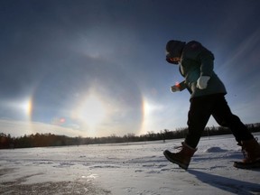 A person walks through Assiniboine Park with sun dogs, properly called parhelia in the background on Friday.