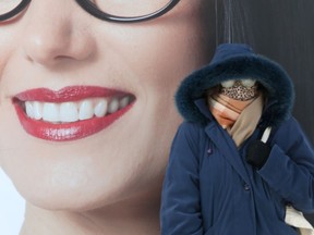 A person with frosted eyeglasses stands in front of a large image depicting a person smiling, in downtown Winnipeg on Saturday.