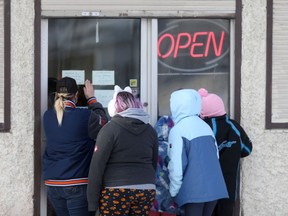 A group of people cluster around the door of a business that has an open sign in the window, in Winnipeg on Tuesday, Feb. 9, 2021. Chris Procaylo/Winnipeg Sun