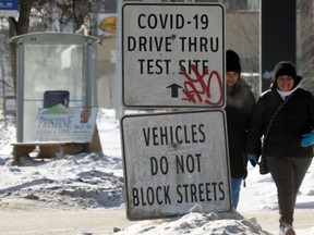 Women walk near a COVID-19 test site sign on Main Street in Winnipeg on Sunday, Feb. 14, 2021.
