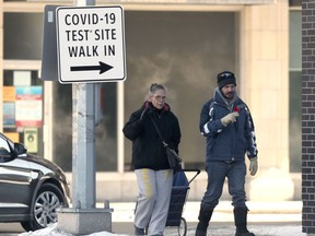 Two people pass a sign for a walk in COVID-19 test site, in downtown Winnipeg on Friday, Feb. 19, 2021.