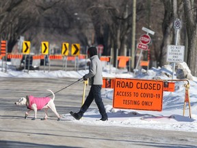 A person with a dog walks past signs for a COVID-19 testing site, in Winnipeg on Saturday.