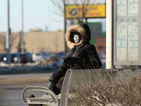 A woman wearing a mask checks to see if her bus is arriving on Regent Avenue in Winnipeg on Sunday.