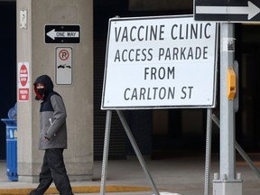 A person wears a mask while walking past a sign for a vaccination clinic, in Winnipeg on Tuesday, Feb. 23, 2021. Chris Procaylo/Winnipeg Sun