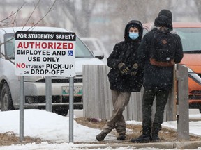 Two people stand near a sign, close to a school, in Winnipeg on Friday, Feb. 26, 2021.
