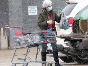 A person wears a mask while loading groceries in to a vehicle in a parking lot, in Winnipeg on Friday, Feb. 26, 2021.