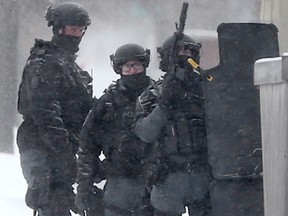 Hiding behind a shield, police conduct an investigation, in Winnipeg on Saturday, Feb. 27, 2021.