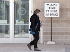 A woman wearing a mask walks past a sign near the COVID-19 vaccination super-site at the Winnipeg Convention Centre in Winnipeg on Sunday, Feb. 28, 2021.