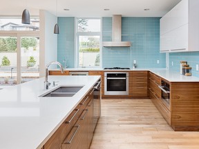 beautiful modern kitchen in new contemporary style luxury home, with island, pendant lights, hardwood floors, and stainless steel appliances. Features blue tone tile that extends to the ceiling