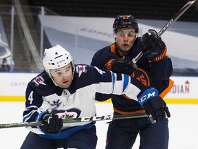 Edmonton Oilers Dominik Kahun (21) and Winnipeg Jets Neal Pionk (4) battle for the puck during first period NHL action on Thursday, March 18, 2021,  in Edmonton. Greg Southam-Postmedia