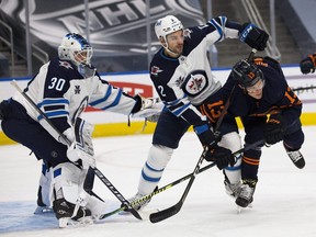Winnipeg Jets goaltender goalie Laurent Brossoit has to deal with Jesse Puljujarvi of the Edmonton Oilers and Jets teammate Dylan DeMelo in front of him on March 18, 2021 in Edmonton.