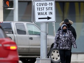 Two people wear masks as they pass a sign for a COVID-19 test site, in Winnipeg on Tuesday, March 2, 2021.