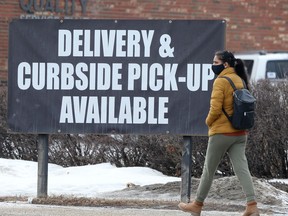 A woman wearing a mask walks past a COVID-19 related sign in Winnipeg on Tuesday. Chris Procaylo/Winnipeg Sun