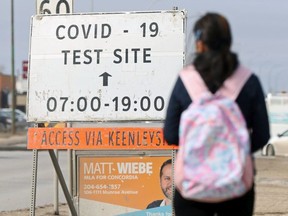 A person walks near a sign for the COVID-19 testing site on Nairn Avenue in Winnipeg on Wed., March 10, 2021.