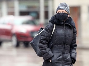 A woman wearing a mask crosses Portage Avenue in Winnipeg on Sunday, March 21, 2021.