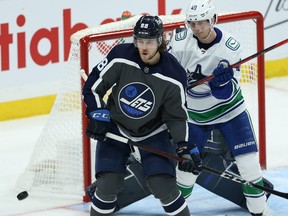 Winnipeg Jets defenceman Nathan Beaulieu (left) positions himself between the puck and Vancouver Canucks centre Elias Pettersson in Winnipeg on Tuesday, March 2, 2021.