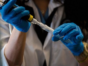 In this file photo Dr. Emilia Liana Falcone simulates tests by adding water into vials at the post-Covid clinic and laboratory at the Institut de Recherches Cliniques de Montreal (IRCM) in Montreal, Quebec on March 3, 2021. -