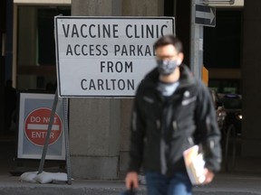 A person wears a mask while walking past a sign for a vaccination clinic in Winnipeg on Thursday.