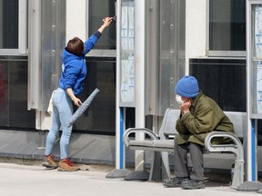 A man sits at a bus stop while a window-washer works in downtown Winnipeg on Mon., April 5, 2021. Kevin King/Winnipeg Sun/Postmedia Network