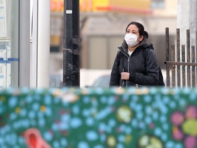 A woman wearing a mask waits at a bus stop in the Osborne Village area of Winnipeg on Monday.