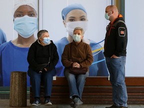 People wear masks while seated in front of a poster depicting people wearing masks, in Winnipeg.   Friday April 16, 2021.