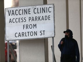 A person wears a mask while walking past a sign for a vaccination centre in Winnipeg.   Tuesday, April 20, 2/2021.Winnipeg Sun/Chris Procaylo/stf