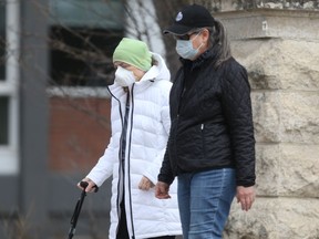 Two people wear masks while walking along a sidewalk, in Winnipeg, during the third wave of COVID-19 on Friday, April 30, 2021.