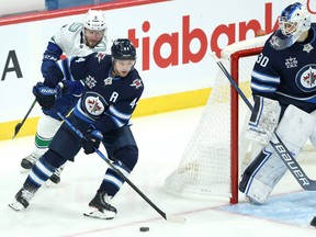 Winnipeg Jets defenceman Josh Morrissey (centre) carries the puck from behind the net with Vancouver Canucks centre J.T. Miller in pursuit on Monday.