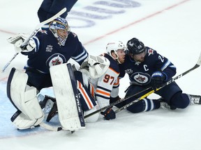 Winnipeg Jets goaltender Connor Hellebuyck (left) is bumped as Edmonton Oilers forward Connor McDavid (centre) and Jets forward Blake Wheeler fall during Game 4 of a Stanley Cup playoff series in Winnipeg on Monday, May 24, 2021.