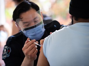 Surrey firefighter Justin Sayson administers a first dose of the Pfizer COVID-19 vaccine to a man at a walk-up vaccination clinic at Bear Creek Park, in Surrey, B.C., on Monday, May 17, 2021.