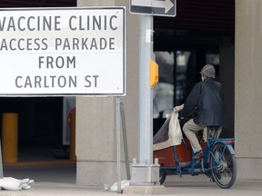 A person cycles by a sign at the COVID-19 vaccination supersite at RBC Convention Centre in Winnipeg on Tuesday, May 4, 2021.