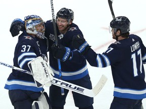 Winnipeg Jets defenceman Tucker Poolman (centre) and Adam Lowry (right) celebrate a sweep of the Edmonton Oilers in a Stanley Cup playoff series with goaltender Connor Hellebuyck in Winnipeg on Monday, May 24, 2021.