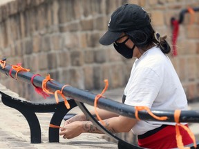 Krystyne Hastings ties an orange ribbon to a post at a memorial to the 215 children killed at a residential school in Kamloops, B.C., at the Oodena Circle at the Forks in Winnipeg, on Sunday, May 30, 2021.