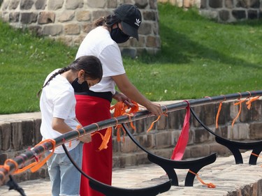 Krystyne Hastings and son Nathan, 8, tie orange ribbons to a post at a memorial to the 215 children killed at a residential school in Kamloops, B.C., at the Oodena Circle at the Forks in Winnipeg, on Sunday, May 30, 2021.