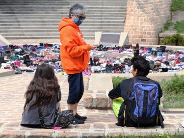 A woman in an Every Child Matters sweatshirt offers ribbons to children sitting at a memorial to the 215 children killed at a residential school in Kamloops, B.C., at the Oodena Circle at the Forks in Winnipeg, on Sunday, May 30, 2021.