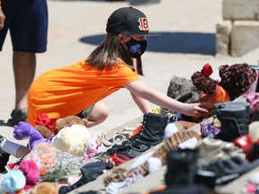 Jordan Flattery-Neumann adds a teddy bear to a memorial for the 215 children who died at the Kamloops residential school, on the steps of the Manitoba Legislative Building in Winnipeg, on Monday, May 31, 2021.