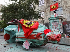 A person stands on a plinth after the defaced statue of Egerton Ryerson, considered an architect of Canada's residential indigenous school system, lies on the pavement after being toppled following a protest at Ryerson University in Toronto, Ontario, Canada June 6, 2021.