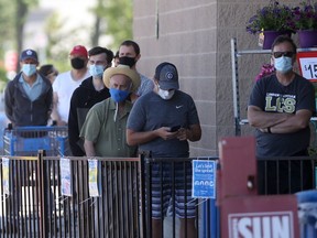 People wear masks while lining up to enter a retail shop, in Winnipeg on Saturday, June 12, 2021.