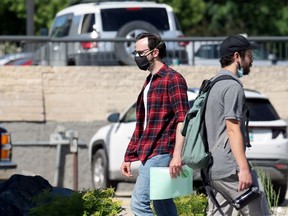 A man wearing a mask (left) with a vaccination sticker on his papers walks past another man with his mask below his chin in the Osborne Village area of Winnipeg on Monday, June 14, 2021.