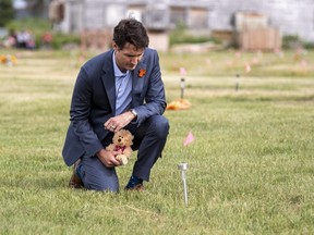 Prime Minister Justin Trudeau lays a teddy bear at a small flag in a field at the site of a former residential school in Cowessess First Nation, Sask., Tuesday, July 6, 2021.