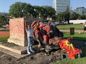 A man poses in front of the toppled Queen Victoria statue at the Manitoba Legislature on Thursday, July 1. The statue, which was covered in red paint, was toppled along with a smaller statue of Queen Elizabeth II as protesters demonstrated against hundreds of unmarked graves found recently at former residential schools in British Columbia and Saskatchewan.