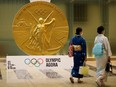 Women wearing protective masks walk past a large-scale reproduction of Tokyo 2020 Olympic Games medal at Nihonbashi Mitsui Tower in Tokyo, Japan, July 14, 2021.