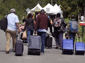 A family from Haiti approach a tent in Saint-Bernard-de-Lacolle, Quebec, stationed by Royal Canadian Mounted Police, as they haul their luggage down Roxham Road in Champlain, N.Y., on August 7, 2017.