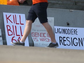 A person walks past signs at the No Truth, No Reconciliation rally Saturday at the Manitoba Legislative Building, in Winnipeg. The rally was against residential school denial, and Bill 64.