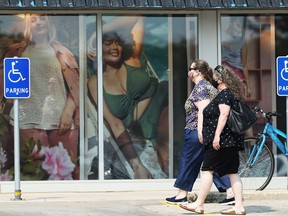 Masked people walk past a retail store window in a Pembina Highway strip mall in Winnipeg on Sunday, July 18, 2021.