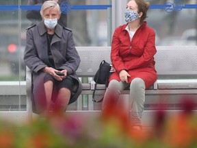 Two people wear masks while sitting at a bus stop in Winnipeg on Tuesday, July 20, 2021.