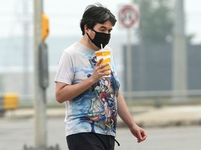 A man wearing a mask carries a beverage while walking along Bishop Grandin Boulevard in Winnipeg on Monday, July 19, 2021.