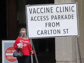 A person wears a mask while walking past a vaccine clinic sign in Winnipeg on Thursday, July 22, 2021.