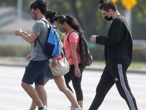 A group of people wear masks while crossing a street in Winnipeg on Saturday, July 24, 2021.