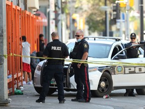 A member of the forensics unit and general patrol officers at a police scene outside the emergency shelter at the Main Street Project on Main Street in Winnipeg on Sunday, July 25, 2021. Police tape blocked the entrance to the building, with a pool of blood and a single evidence marker just outside the door.